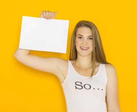 Nice young attractive woman holding blank paper and point on it. Mockup template for your design with copy space on orange backgroundの写真素材