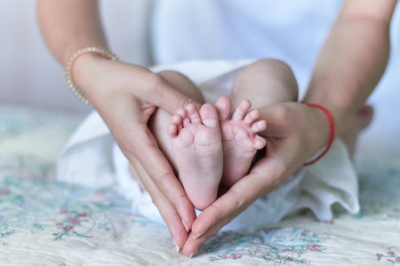 Baby's small feet, in the symbolic shape of a heart, woven from beautiful female hands, wrapped in care and loveの写真素材