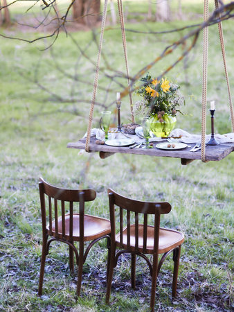 Still life of a suspended table set for a meal, decorated with a bouquet of flowers, vintage chairs,...