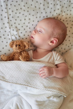 A charming baby is sleeping peacefully in his crib in an embrace with his favorite toy