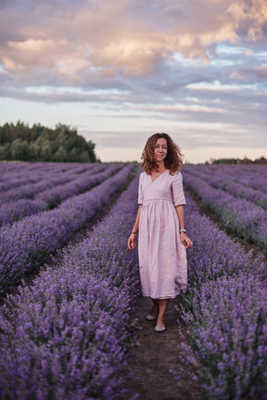 Beautiful young woman walking in lavender field at sunset, summer eveningの写真素材