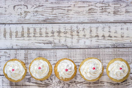 cupcakes with white cream with a heart on a white wooden backgroundの写真素材