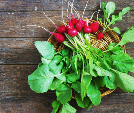 Fresh radishes on old wooden table in a wicker basketの写真素材