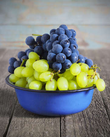 blue and green grapes in a metal bowl on a wooden backgroundの写真素材