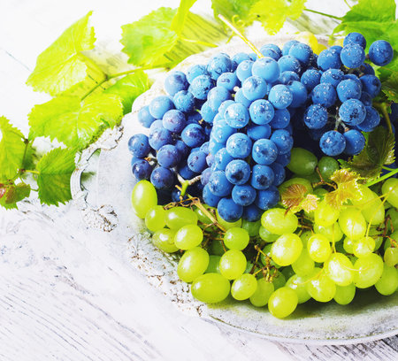 blue and green grapes in a basket on a white wooden background  toningの写真素材