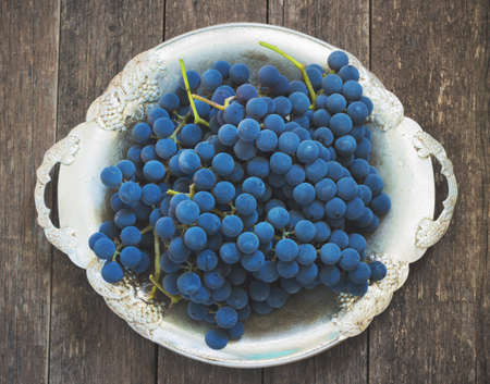 blue grapes in a metal bowl on a wooden backgroundの写真素材