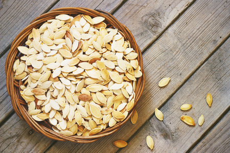 Salted pumpkin seeds on a rustic wooden background in a wicker basketの写真素材