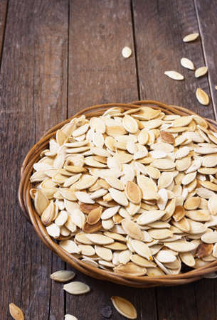 Salted pumpkin seeds on a rustic wooden background in a wicker basketの写真素材