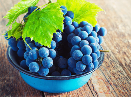 blue and green grapes in a metal bowl on a wooden background  toning
