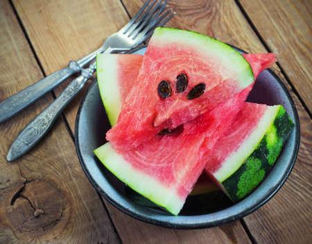 slices of watermelon in a metal bowl on a wooden backgroundの写真素材