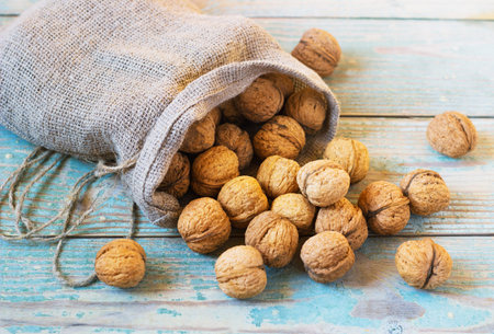 Pile of walnuts in shellin a bag on a wooden background . Linen sack with walnuts in the background.