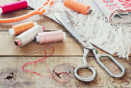Scissors, bobbins with thread and needles, striped fabric. Old sewing tools on the old wooden background. Vintage Background toningの写真素材