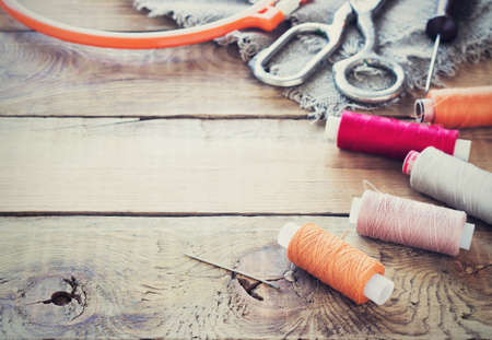 Scissors, bobbins with thread and needles, striped fabric. Old sewing tools on the old wooden background. Vintage Background toningの写真素材