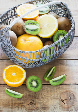 Fresh juicy citrus fruits in a basket on a wooden background kiwi, orange, lemon, grapefruitの写真素材