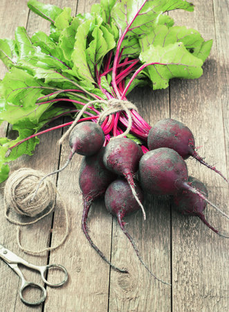 Young,fresh beets with tops on old wooden background.Style rustic toning