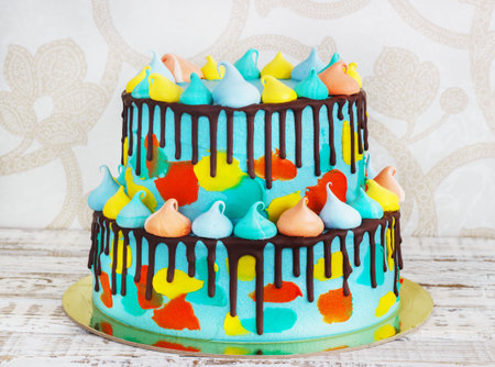 2-tiered homemade childrens cake decorated with colorful daub with meringue on white background