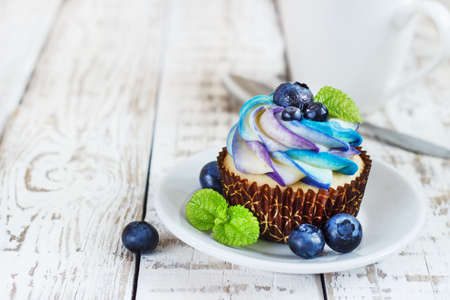 Delicate vanilla cupcakes with cream and berries on a white wooden backgroundの写真素材