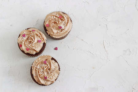 Chocolate cupcakes decorated with cream rose with hearts on a white wood backgroundの写真素材