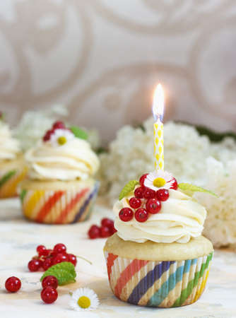 Gentle cupcake with cream and berries nd a candle a light backgroundの写真素材