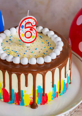 bright birthday cake with chocolate on a light background with balloonsの写真素材