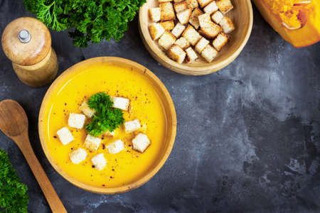 Pumpkin soup with cream, bread and fresh parsley in a rustic metal plate over grunge black background. Top view, copy spaceの写真素材