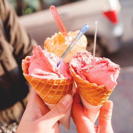 Three colorful tasty ice-cream cones in hands. Sunny background with cold desserts in hands of...