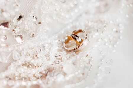 Golden wedding rings on lace silk fabric with beads. Wedding embroidery dress detail.の写真素材