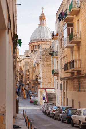 VALLETTA, MALA - February 20, 2010 - Ancient street in Valletta, Malta. Narrow street with old fashioned balcony, carved stone walls and the St. Pauls Cathedral at the end of street.のeditorial素材