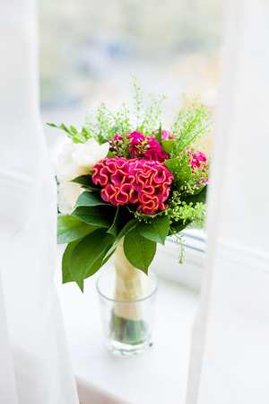 Wedding bouquet on window sill. Bride's traditional symbolic accessory. Floral composition with red celosia flowers.の写真素材