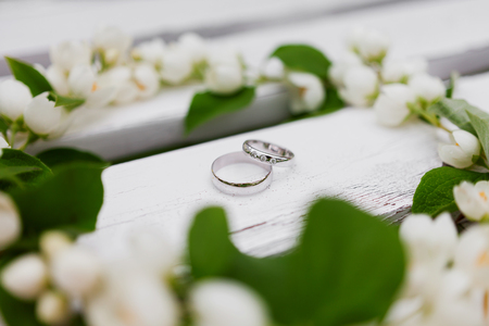 Golden wedding rings with diamonds lie inside jasmine (Philadelphus) flower in bridal bouquet. Symbol of love and marriage. Wedding bouquet. Bride's traditional symbolic accessory. Floral composition with jasmine flowers.の写真素材