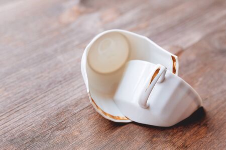 Broken white cup on wooden background. Damaged mug with golden decoration.の写真素材