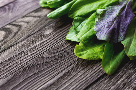 Fresh leaves of sorrel and salad on wooden background. Rustic table with green and violet edible...