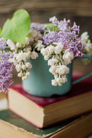 Two old books and rusty mug with lilac bouquet on homespun napkin. Interesting reading, vintage background.の写真素材