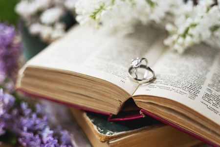 Pair of wedding rings with diamond. Rustic background with old books and lilac flowers. Retro background. Selected soft focus.の写真素材