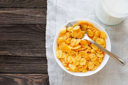 Tasty corn flakes in bowl with bottle of milk. Rustic wooden background with homespun napkin. Healthy crispy breakfast snack. Place for text. Top view, flat lay.の写真素材