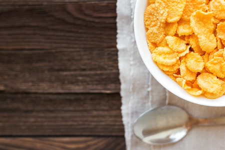 Tasty corn flakes in bowl. Rustic wooden background with homespun napkin. Healthy crispy breakfast snack. Place for text. Top view, flat lay.の写真素材