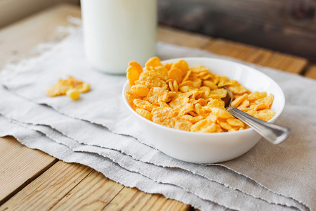 Tasty corn flakes in bowl with bottle of milk. Rustic wooden background with homespun napkin. Healthy crispy breakfast snack.の写真素材