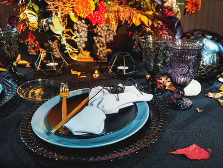 Table served in Halloween style. Bouquet with red flowers, decorative spiders, pumpkins with lettering and gothic vine glasses on black tablecloth. Holiday decorations.の写真素材