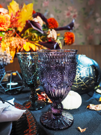 Table served in Halloween style. Bouquet with red flowers, decorative spiders, pumpkins with lettering and gothic vine glasses on black tablecloth. Holiday decorations.の写真素材