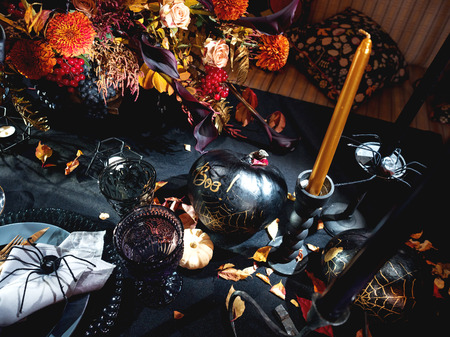 Table served in Halloween style. Bouquet with red flowers, decorative spiders, pumpkins with lettering and gothic vine glasses on black tablecloth. Holiday decorations.の写真素材