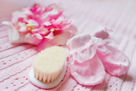 First accessories for newborn girl - pink booties, hat with silk flower and tiny hair brush. Cute pink background.の写真素材