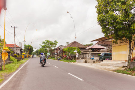 UBUD, INDONESIA - January 26, 2013. Religious decoration near houses on street. Road traffic in cloudy day.のeditorial素材