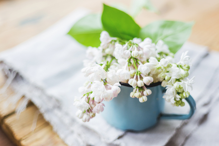 Lilac (Syringa) flowers in old rusty mug. Spring background with white and violet flowers in rustic cup on wooden table.の写真素材
