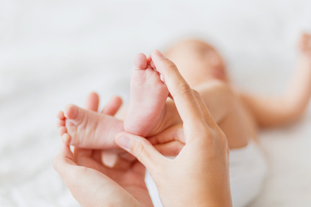 Mother holds newborn baby's bare feet. Tiny feet in woman's hand. Cozy morning at home.の写真素材