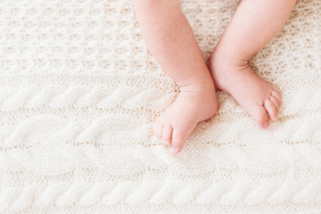 Baby's feet on white knitted background. Little child's bare feet. Cozy morning bedtime at home. Place for text.の写真素材