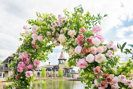 Beautiful floral arch for wedding ceremony. Vases with pink roses and peonies. Wedding set up outdoors in park near pond.の写真素材