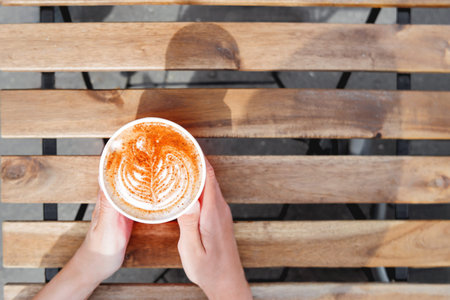Woman holding a paper cup with coffee. Coffee to go. Tasty hot beverage on wooden table in sunny...