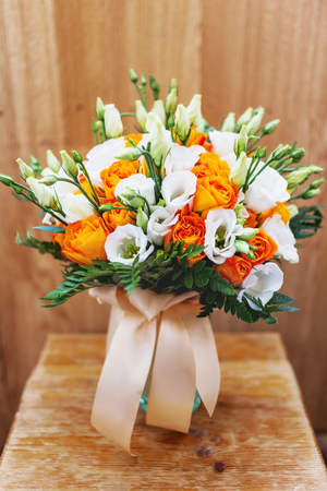 Wedding bouquet on shabby wooden background. Bride's traditional symbolic accessory. Floral composition with eustoma (or Lisianthus) and orange roses.の写真素材