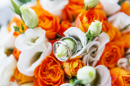 Pair of golden wedding rings inside bridal bouquet. Symbol of love and marriage on orange roses and eustoma (or Lisianthus). Traditional bride's accessory.の写真素材