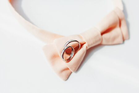 Pair of golden wedding rings lies on peach colored bow tie. The traditional accessories of the groom at the wedding.の写真素材